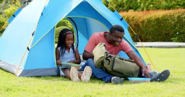 Afro-Amerikalı, baba-kız çadırda piknik yapıyor, gülümsüyor ve dışarıda atıştırmalıkları paylaşıyor. Aile, bağ, doğa, kamp, boş zaman, birliktelik.