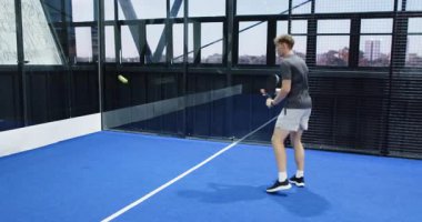 Young man playing padel tennis on blue indoor court, preparing to hit ball. sport, racket, athletic, competition, game, practice