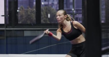 Padel tenis oynayan odaklanmış bir kadın, sahada yoğun bir maça hazırlanıyor. Spor, rekabet, atletizm, antrenman, konsantrasyon, raket