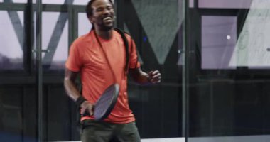 Turuncu tişörtlü sporcu Padel tenis oynuyor, maça odaklanıyor, kapalı sahada. Spor, rekabetçi, raket, fitness, egzersiz, aktif