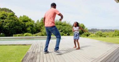 Afrikalı Amerikalı, baba ve kızı yemyeşil bahçede ahşap güvertede neşeyle dans ediyorlar. Aile, bağ, mutluluk, yaşam tarzı, haftasonu, rahatlama