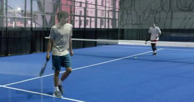 Kapalı sahada Padel tenis oynayan genç adam, topa odaklanıyor. Spor, raket, eylem, kararlılık, atlet