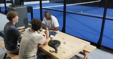 Farklı arkadaşlar tenis maçından sonra kutlama yapıyorlar, kapalı sahada birlikte vakit geçiriyorlar. Kutlama, dostluk, spor, raket, rekabet, eğlence