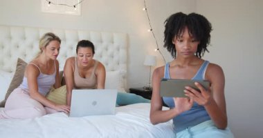 Çeşitli bayan arkadaşlar yataklarında, dizüstü bilgisayar ve tablet kullanıyorlar, evde boş vakitlerin tadını çıkarıyorlar. dostluk, teknoloji, dijital cihazlar, bağlanma, gündelik, yaşam tarzı