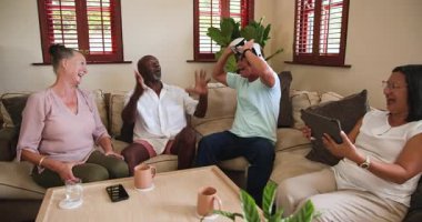 Çeşitli yaşlılar evde birlikte gülüyor, sanal gerçekliğin ve sohbetin tadını çıkarıyorlar. kahkaha, teknoloji, kulaklık, yaşlılık, eğlence, eğlence