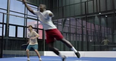 Kapalı alanda tenis oynayan çeşitli adamlar yoğun bir maça odaklanıyorlar. Spor, rekabet, takım çalışması, raket, atletik, egzersiz