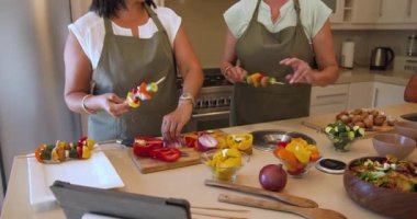 Çeşitli kadınlar mutfakta renkli sebze şişleri hazırlıyor, evde birlikte yemek pişirmekten zevk alıyorlar. Mutfak, takım çalışması, sebze, hazırlık, mutfak, arkadaşlık