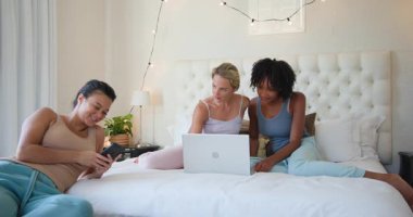 Çeşitli bayan arkadaşlar yataklarında dizüstü bilgisayar kullanıyor ve mutlu bir şekilde sohbet ediyorlar. Arkadaşlık, kaynaşma, teknoloji, eğlence, sohbet, kadınlar.