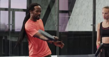 Young woman practicing padel tennis swing with coach in modern indoor court. coaching, racquet, sports, fitness, training, teamwork