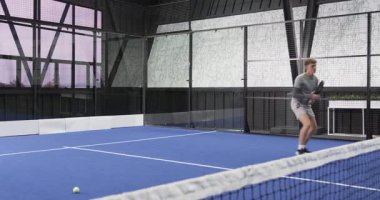 Padel tenisi oynayan genç adam, kapalı alanda topa vurmaya hazırlanıyor. Spor, egzersiz, fitness, raket, aksiyon, rekabetçi