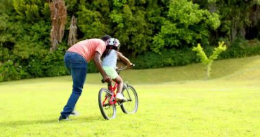 Afrikalı Amerikalı, babası kızına parkta bisiklet sürmeyi öğretiyor, açık havada kaynaşmanın tadını çıkarıyor. Ebeveynlik, aile, çocukluk, eğlence, öğrenme, açık hava