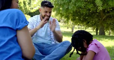 Family enjoying clapping game together in sunny park, smiling and bonding. outdoors, leisure, togetherness, playful, happiness, recreation