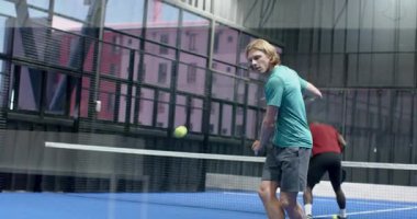 Padel tenisi oynayan genç adam, kapalı sahada topa vurmaya odaklanıyor. Spor, raket, atletik, konsantrasyon, raket, aksiyon