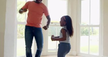 Afro-Amerikan, baba-kız evlerinde büyük pencerelerin yanında neşeyle dans ediyorlar. Aile, bağ, mutluluk, dans, eğlence, ebeveynlik