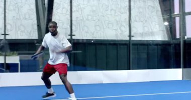 Padel tenis oynayan genç bir adam, kapalı sahada raket sallıyor. Spor, fitness, yarışma, atlet, pratik, çeviklik