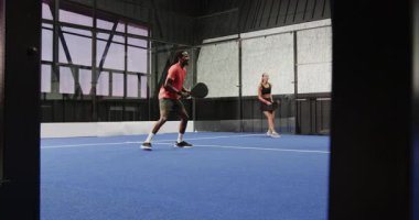 Mavi kortta Padel tenis oynayan, gülümseyen ve oyundan zevk alan bir adam. Spor, egzersiz, raket, hobi, rekabet, aktif