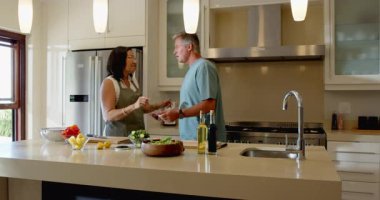 Modern mutfakta, tezgahta ve evde taze salatayla neşeyle dans eden kıdemli çift. Yaşam tarzı, sağlıklı yaşam, aktif, mutluluk, ilişki, aşçılık