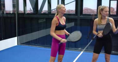 Padel tenis oynayan, gülümseyen ve içeride raket tutan kadınlar. Takım çalışması, egzersiz, spor, eğlence, arkadaşlık