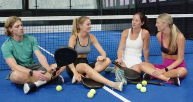 Bir grup arkadaş kapalı sahada raketler ve toplarla Padel tenis stratejisini tartışıyorlar. Spor, takım çalışması, eğlence, aktivite, açık hava, oyun