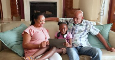 Farklı büyükbabalar ve torunlar kanepede birlikte tablet kullanırlar, ailecek vakit geçirmenin tadını çıkarırlar. Bağlanma, teknoloji, birliktelik, oturma odası, mutluluk