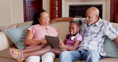 Farklı büyükbabalar ve torunlar kanepede birlikte tablet kullanırlar, evde ailece vakit geçirmenin tadını çıkarırlar. teknoloji, bağ, nesiller, birliktelik