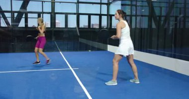 Kapalı sahada Padel tenis oynayan kadınlar, rekabetçi maçlara odaklanıyorlar. Spor, raket, rekabet, takım çalışması, eğlence, spor