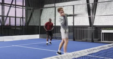 Kapalı alanda tenis oynayan iki farklı adam yoğun bir maça odaklanıyor. Spor, rekabet, takım çalışması, raket, dinamik, atlet