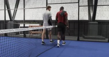 İki farklı adam kapalı sahada tenis maçına hazırlanıyor, ellerinde raketler var. Spor, egzersiz, fitness, takım çalışması, rekabet, dayanıklılık