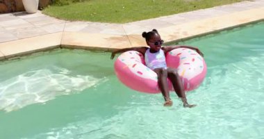 Havuzda dinlenen çocuk, güneşli gökyüzünün altında pembe şişme bir yüzüğün üzerinde yüzüyor. Havuz kenarı, yaz tatili, tatil, yüzme, güneş ışığı.