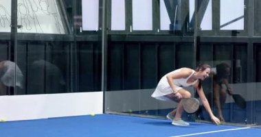 Kapalı sahada Padel tenis oynayan odaklanmış bir kadın elinde raketle hizmet etmeye hazır bekliyor. Spor, eğlence, atletizm, rekabet, raket, kadın