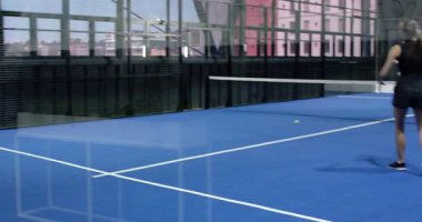 Kapalı alandaki mavi sahada Padel tenis oynayan genç sporcular, odaklanmış ve enerjik. Spor, rekabet, takım çalışması, raket, dinamik, eğitim