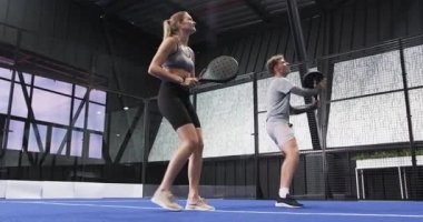 Genç adam ve kadın kapalı sahada Padel tenis oynuyorlar, rekabetin tadını çıkarıyorlar. Spor, eğlence, fitness, takım çalışması, raket, yaşam tarzı