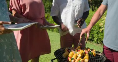Bahçede mısır ve sebze ızgara, çeşitli kıdemli arkadaşlar yaz barbeküsünün tadını çıkarıyorlar. piknik, yaz zamanı, toplanma, yemek pişirme, yemek hazırlama