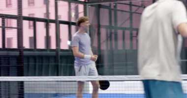 Padel tenis maçından zevk alan genç erkekler, kapalı sahada gülüyor ve birbirlerine destek oluyorlar. Spor, takım çalışması, arkadaşlık, eğlence, spor, aktif yaşam tarzı