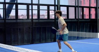 Genç adam kapalı sahada tenis oynuyor, gülümsüyor ve raket tutuyor. Spor, raket, atlet, eğlence, rekabet, egzersiz