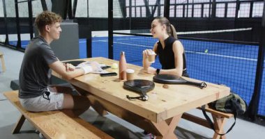 Padel tenis kortunda strateji tartışan genç sporcular ellerinde raketler ve içkilerle. Spor, takım çalışması, susuzluk, iletişim, aktif yaşam tarzı, rekabet