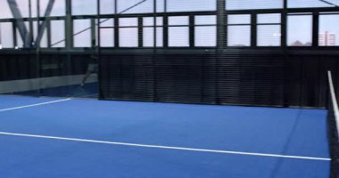 Büyük pencerelerden mavi zemin ve şehir manzaralı boş padel mahkeme salonu. Spor, mimari, şehir, eğlence, eğlence, raket