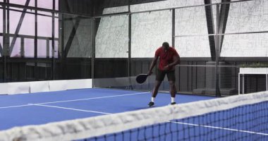 Afrika kökenli Amerikalı bir adam kapalı sahada tenis oynuyor, odaklanmış ve hazır. Spor, raket, atlet, yarışma, aksiyon, fitness