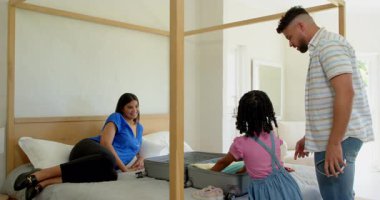 Aile bavullarını yatağa topluyor, tatili heyecanla ve gülümsemeyle hazırlıyor. Seyahat, bagaj, tatil, hazırlık