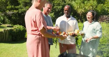 Bahçe barbeküsünde eğlenen, sebze ızgara yapan ve birlikte gülümseyen kıdemli arkadaşlar. Arkadaşlık, toplanma, yemek pişirme, boş zaman, yaşam tarzı