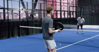 İki farklı adam kapalı alanda tenis oynuyor, odaklanmışlar ve harekete geçmeye hazırlar. Spor, rekabet, takım çalışması, egzersiz, raket, maç