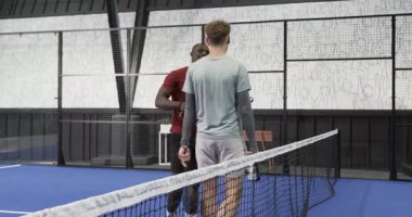 Kapalı sahada Padel tenis maçına hazırlanan iki farklı adam strateji tartışıyorlar. Spor, takım çalışması, raket, iletişim, işbirliği, ortaklık