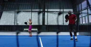 Padel tenisi oynayan bir kadın, topa vurmaya hazırlanan bir kadın, kapalı alanda dalış yapan bir rakip. Spor, rekabet, raket, takım çalışması, çeviklik, eylem