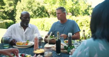 Bahçe yemeklerinde eğlenen çeşitli yaşlılar güneşli bahçe ortamında yemek ve kahkaha paylaşıyorlar. Yaşlı, bahçede, piknik, mutluluk, boş zaman, yemek