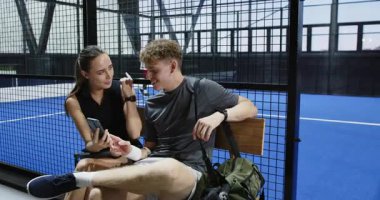 Yedek kulübesinde dinlenen genç sporcular maçtan sonra kapalı sahada Padel tenis stratejisini tartışıyorlar. Spor, tartışma, takım çalışması, egzersiz, eğlence, eğitim