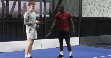 İki farklı adam kapalı alanda tenis oynuyor, kapalı sahada rekabetçi oyun aksiyonlarına odaklanıyor. Spor, rekabet, takım çalışması, raket, atletizm, iç saha