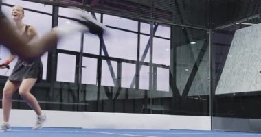 Çeşitli oyuncular kapalı sahada yoğun bir Padel tenis maçının keyfini çıkararak eyleme odaklanıyor. Spor, rekabet, takım çalışması, eğlence, raket, eğlence.