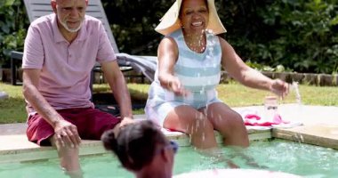 Farklı büyükbabalar, torunlarıyla havuzda güneşli bir günün tadını çıkarıyorlar. Aile, kaynaşma, yaz tatili, tatil, rahatlama, dinlenme.