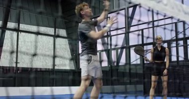 Çeşitli oyuncular kapalı sahada yoğun bir Padel tenis maçına katılıyor ve hareketlerine odaklanıyor. Spor, atletizm, rekabet, raket, takım çalışması, fitness