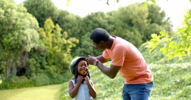 Afro-Amerikan, baba-kız açık havada eğleniyor, bisiklet kaskını paylaşıyorlar. Aile, babalık, bisiklet, birliktelik, eğlence.